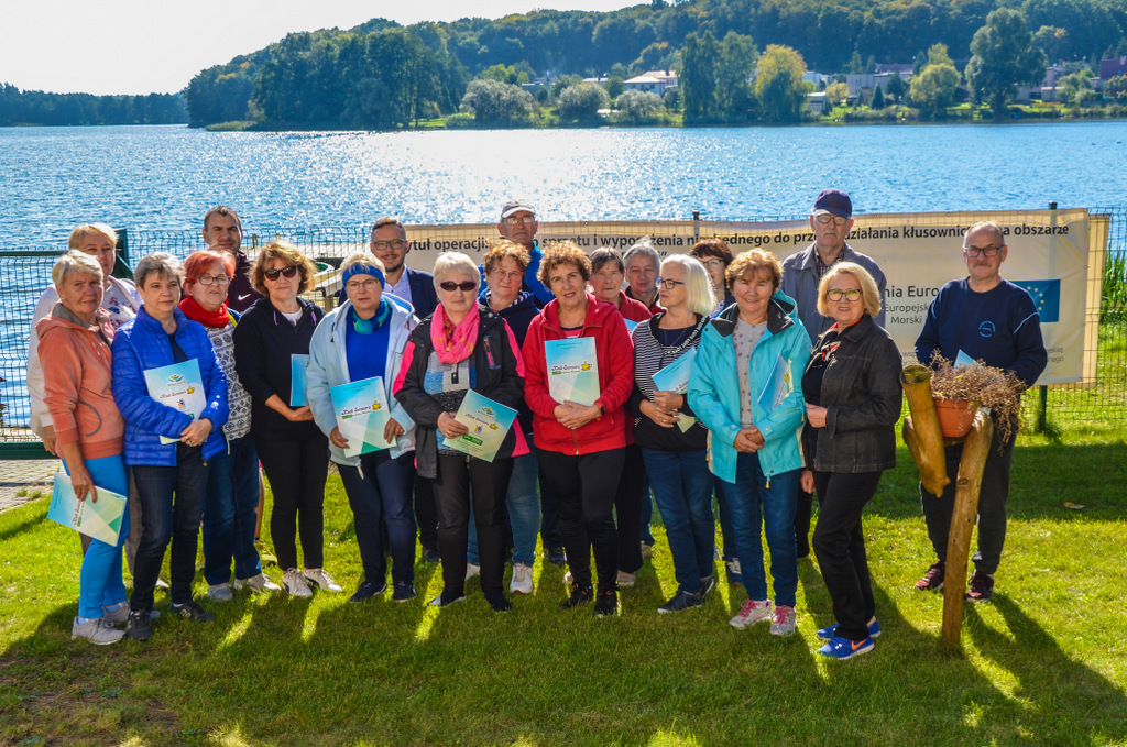 Zdjęcie główne przedstawia grupę seniorów biorących udział w zajęciach nordic walking po wręczeniu certyfikatów.